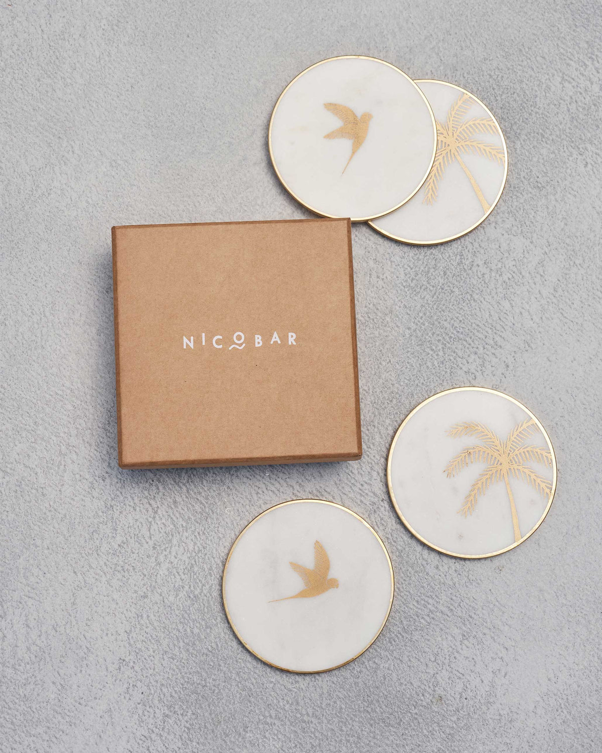 Coastline coasters around a kraft gift box, with gold palm and bird motifs.