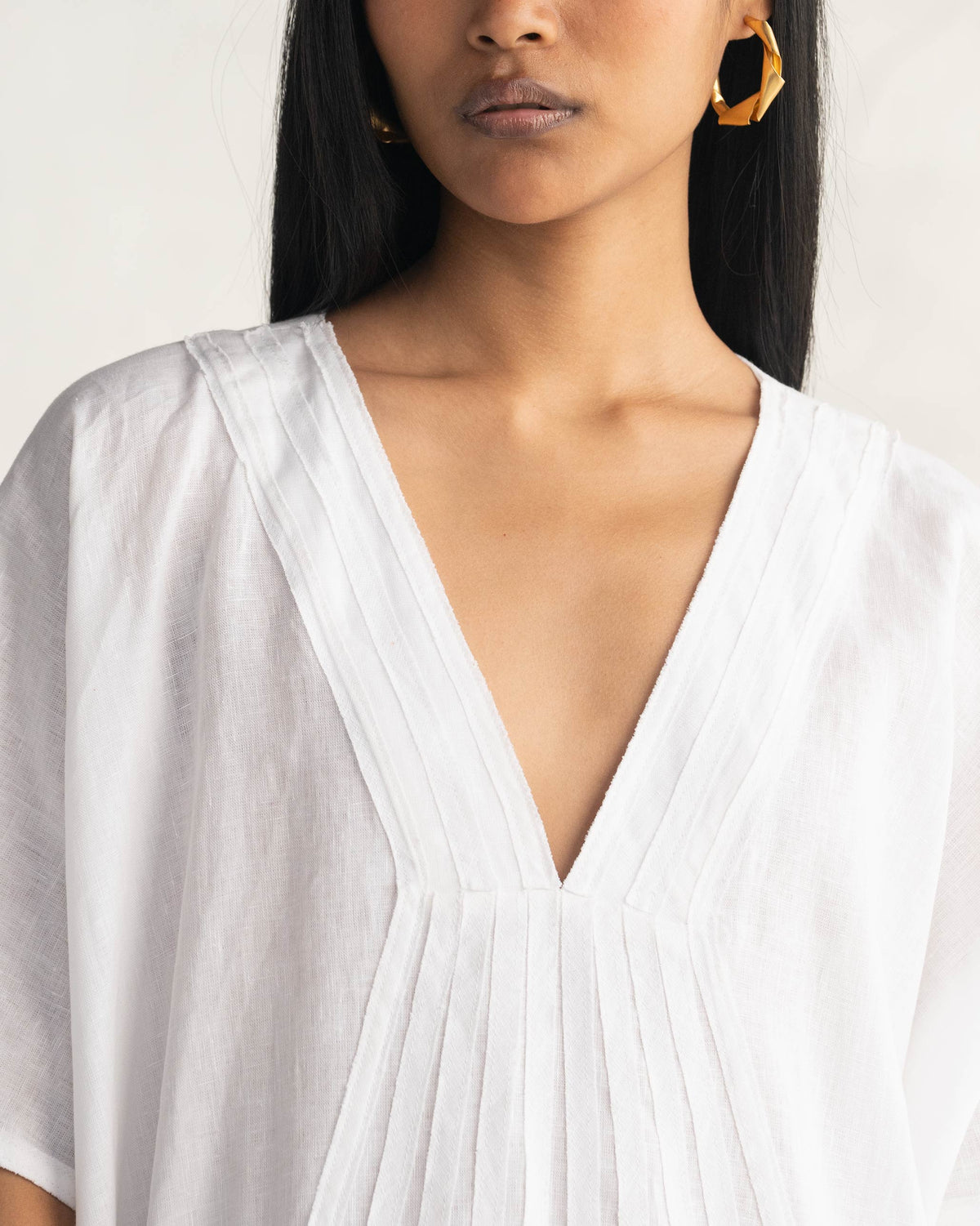 Close-up of pintuck detailing along the V-neck of a white Tulum kaftan.