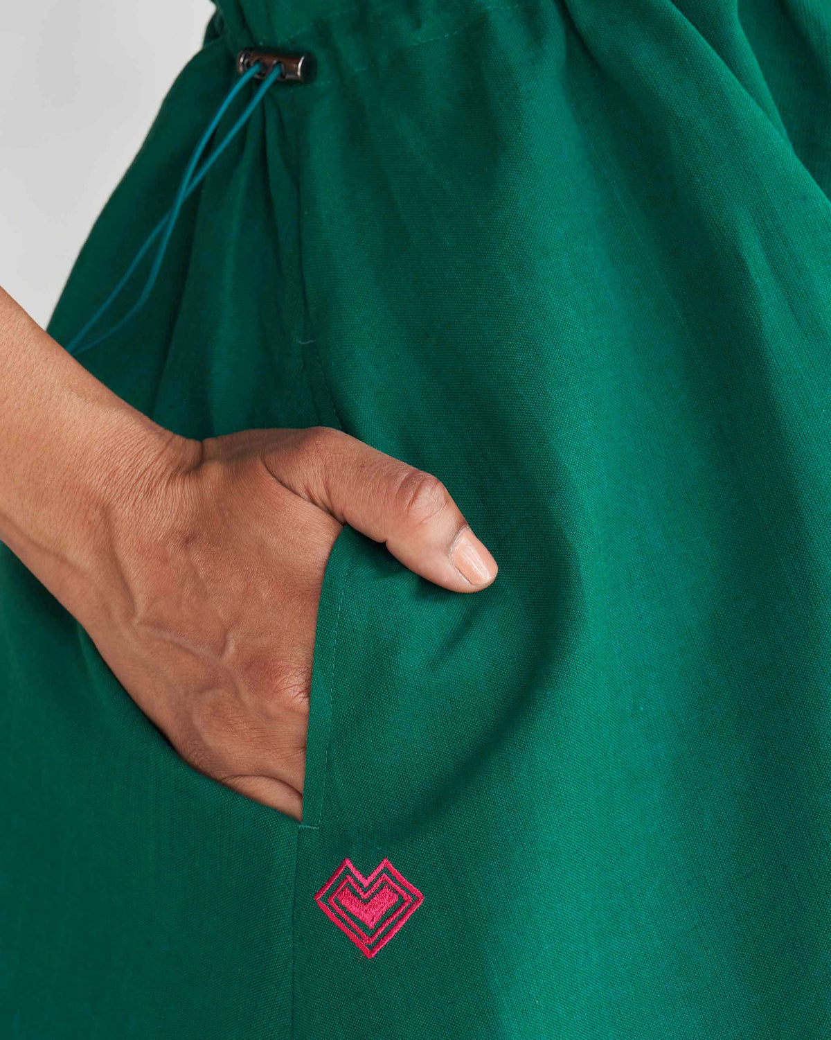 Close-up of a green Midori dress pocket with a pink heart embroidery.
