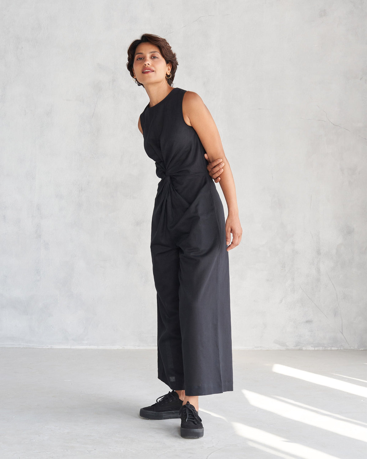 Person wearing a black Front Knot Jumpsuit with a twisted waist, turned to one side.