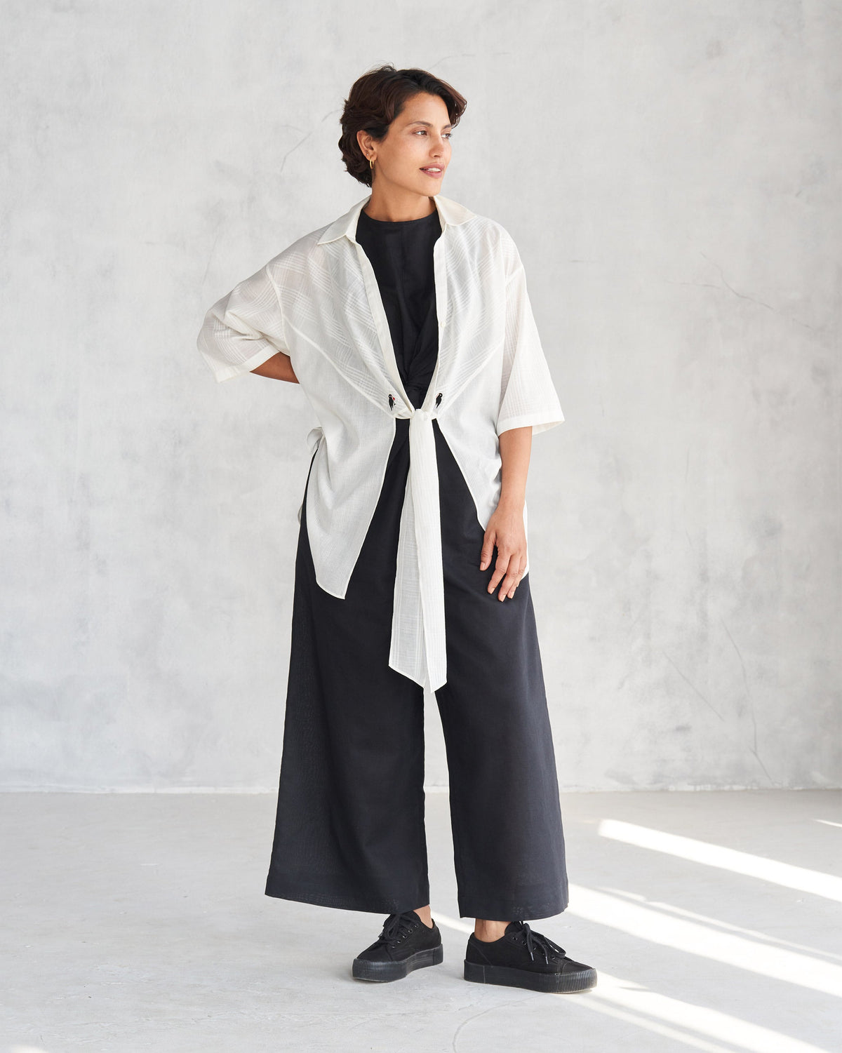 Person wearing a black Front Knot Jumpsuit under a white shirt tied at the waist.