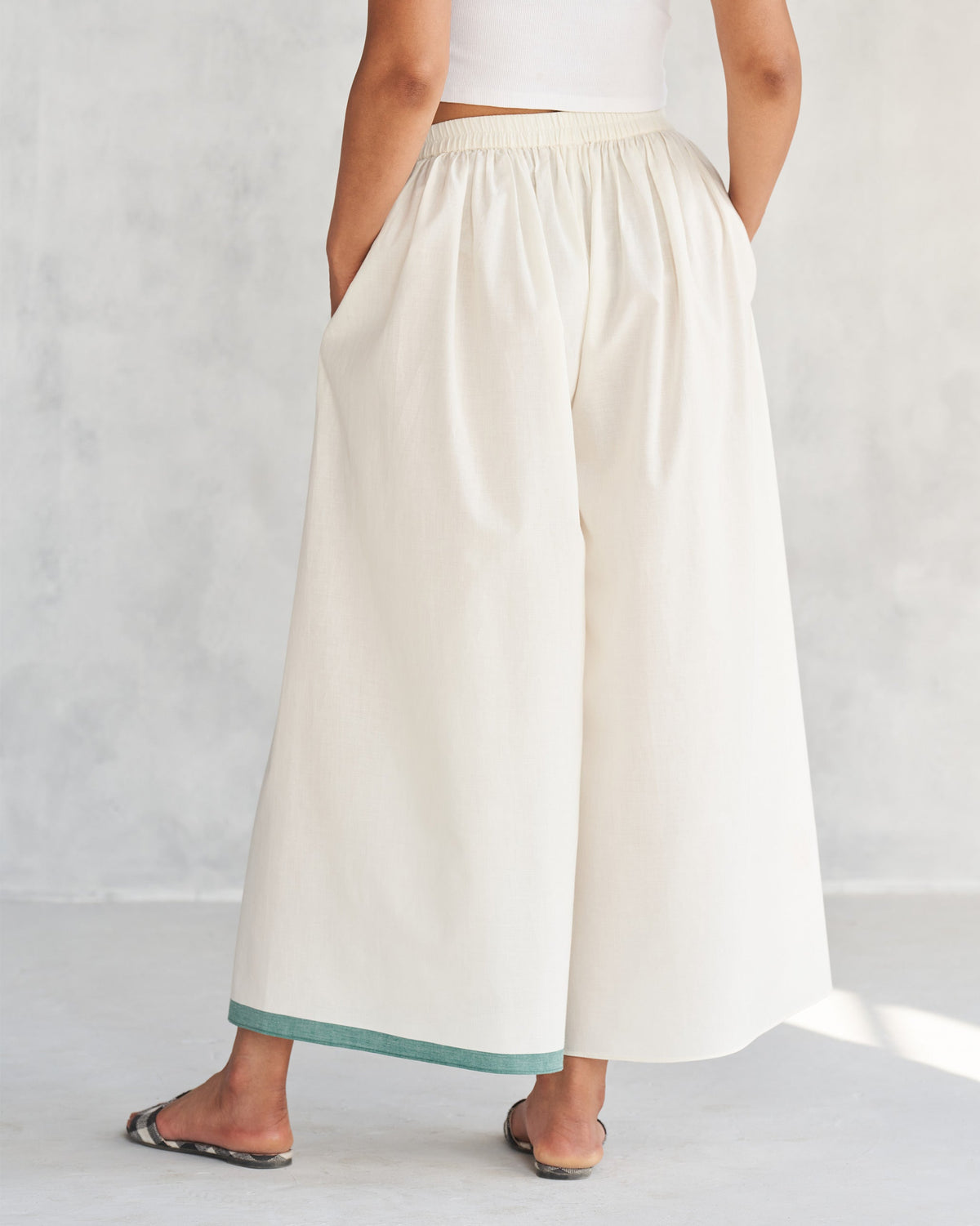 Back of ivory Shiro Hem Pants with a teal hem band worn by a person.