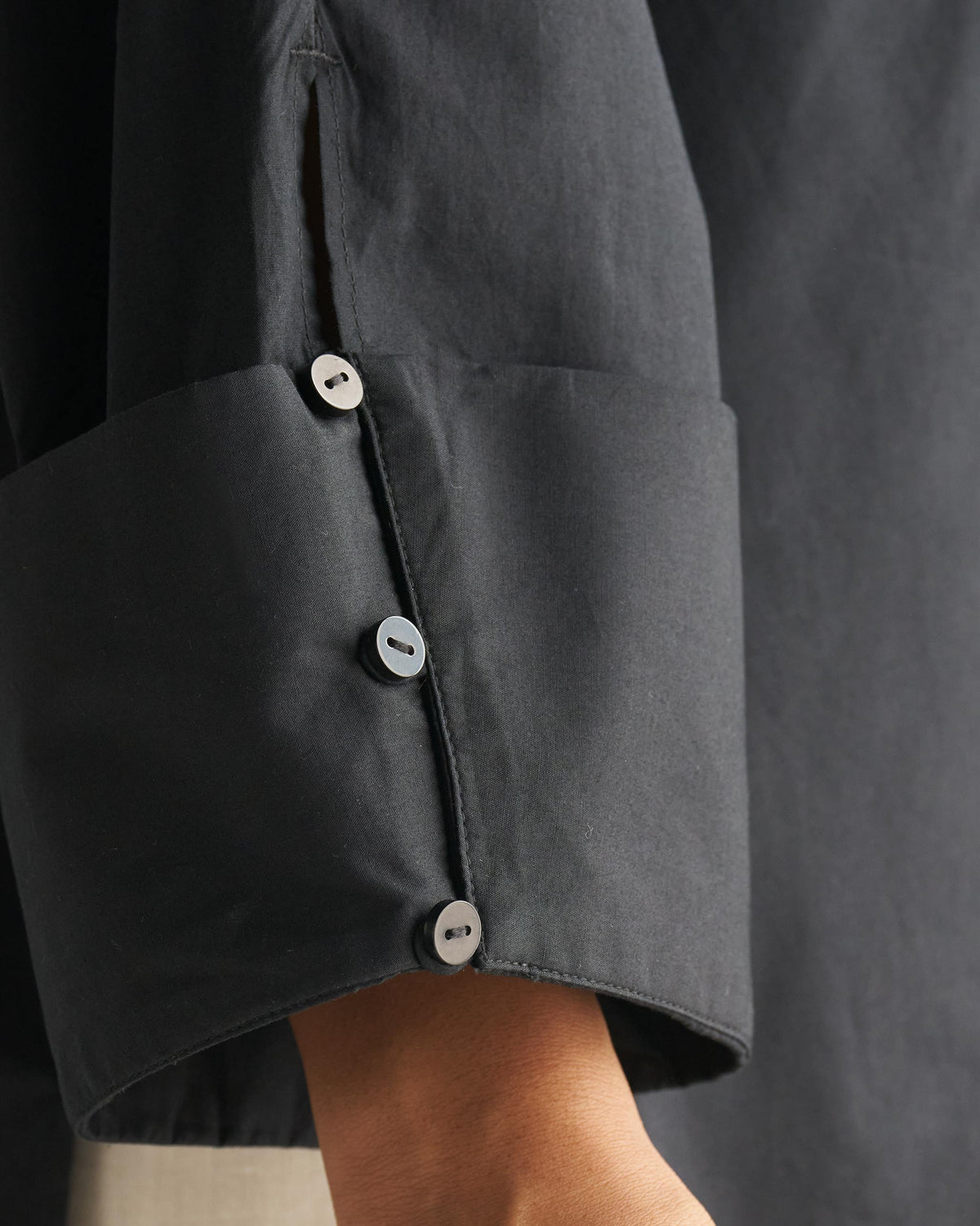 Close-up of a black Cirrus shirt cuff with three dark buttons.