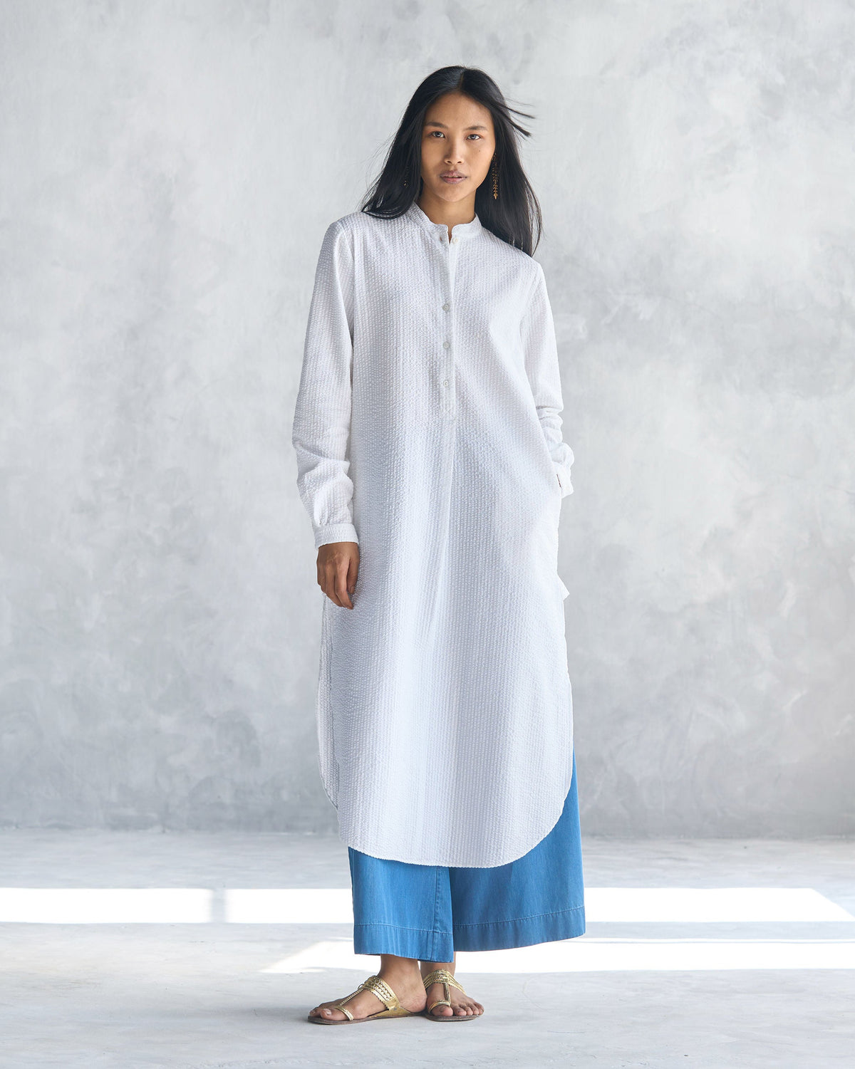Person wearing a white seersucker long kurta with side slits.