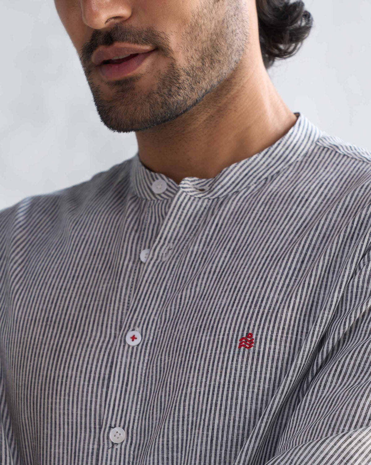 Close-up of a charcoal stripe Nawab shirt showing a small red embroidered motif on the chest.