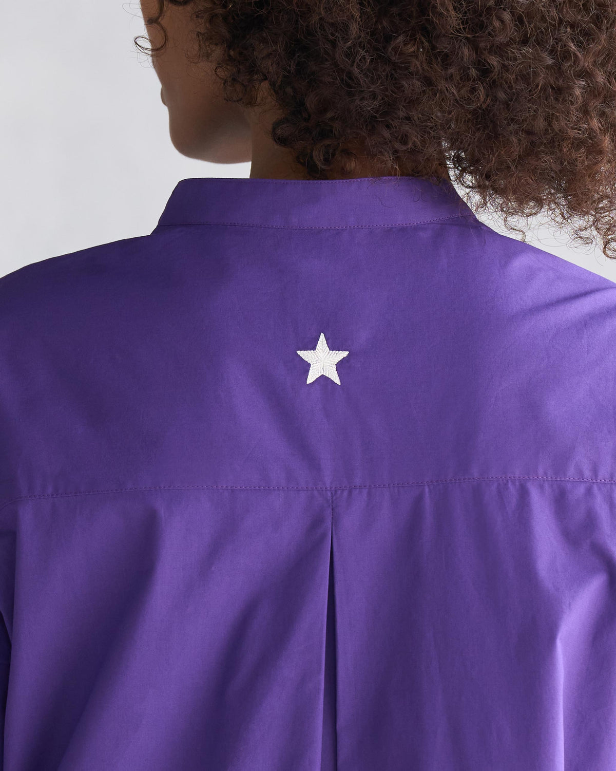 Back of a purple Pema top with a band collar and a white star embroidery.