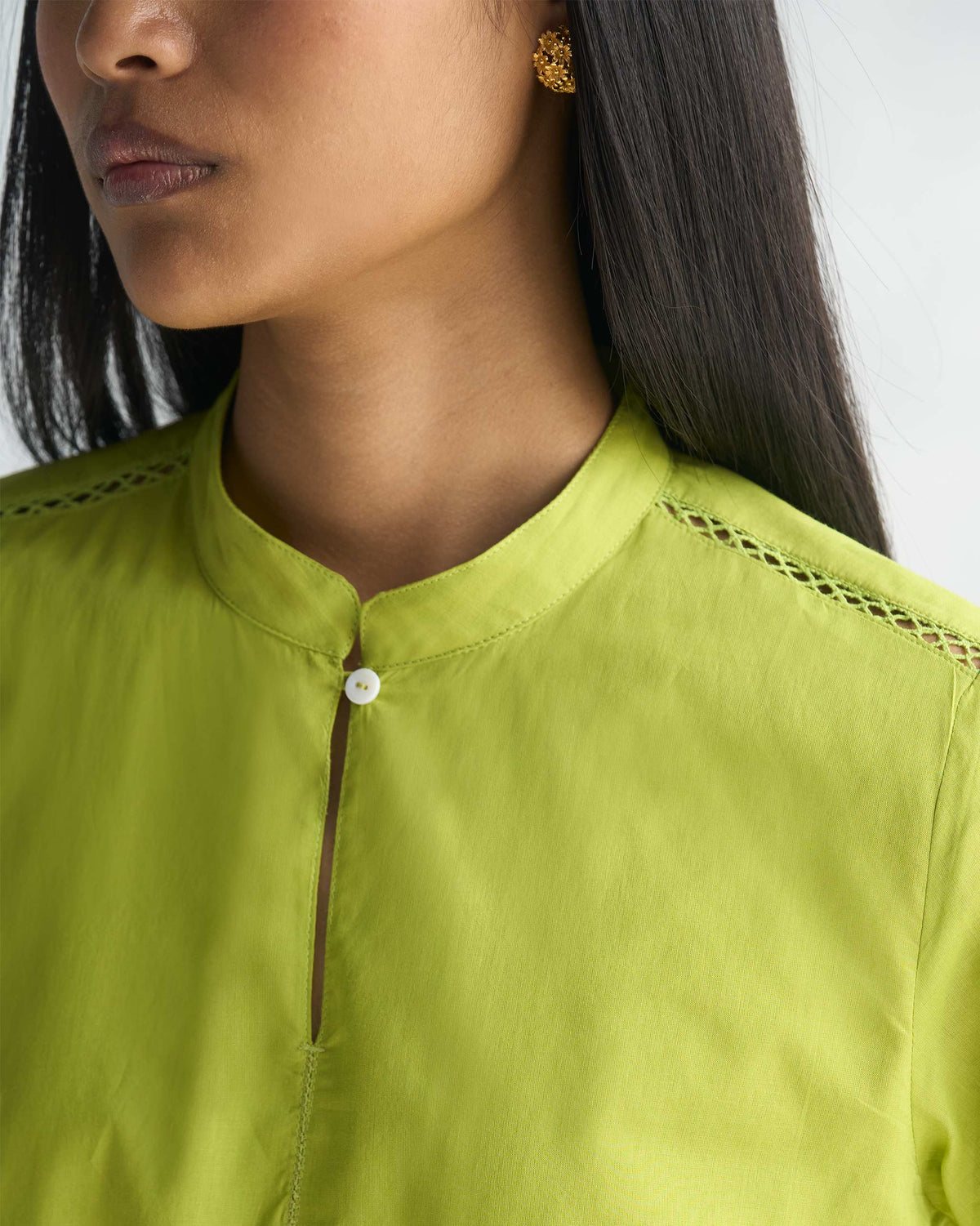 Close-up of a lime kurta's stand collar with a white button and lattice trim at the shoulders.