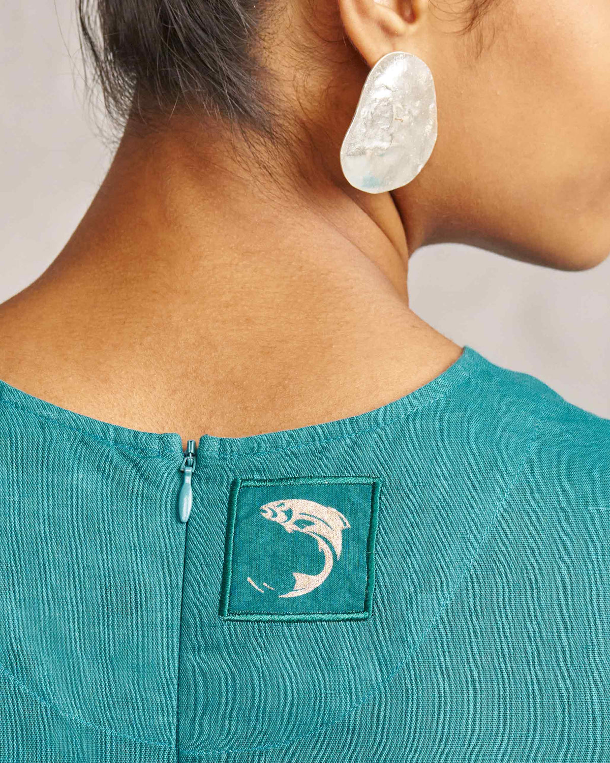 Close-up of the Front Knot Jumpsuit neck label showing a fish motif.