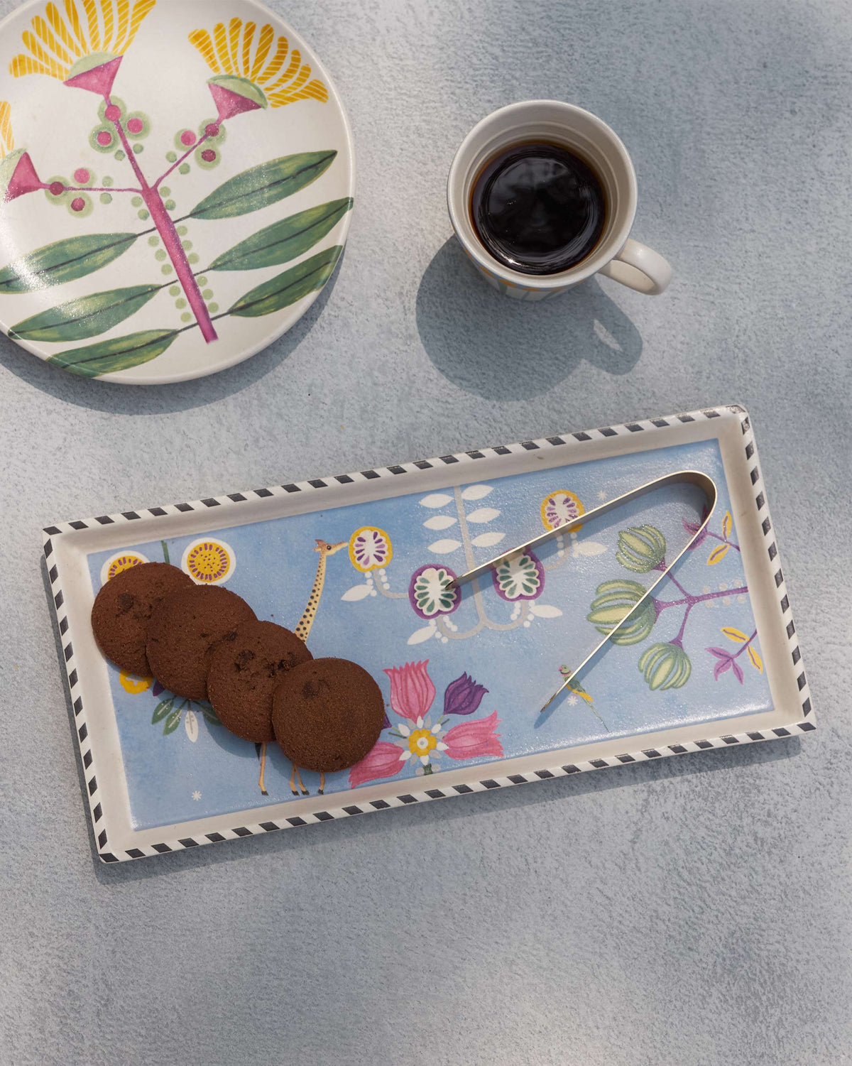 Flat-lay of the Bahari Cookie Tray with its tong laid across the design.