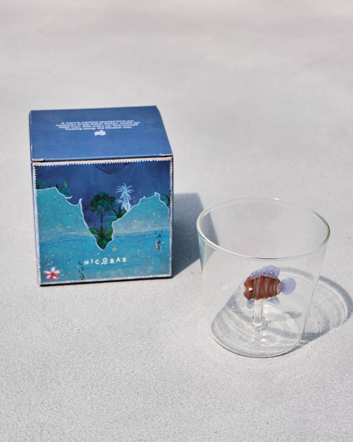 Angelfish Glass with a striped orange glass fish, beside a blue Nicobar box.