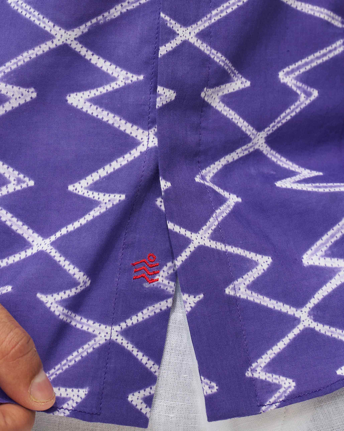 Close-up of a purple Riverine shirt hem showing a small red wave motif embroidered on the front.