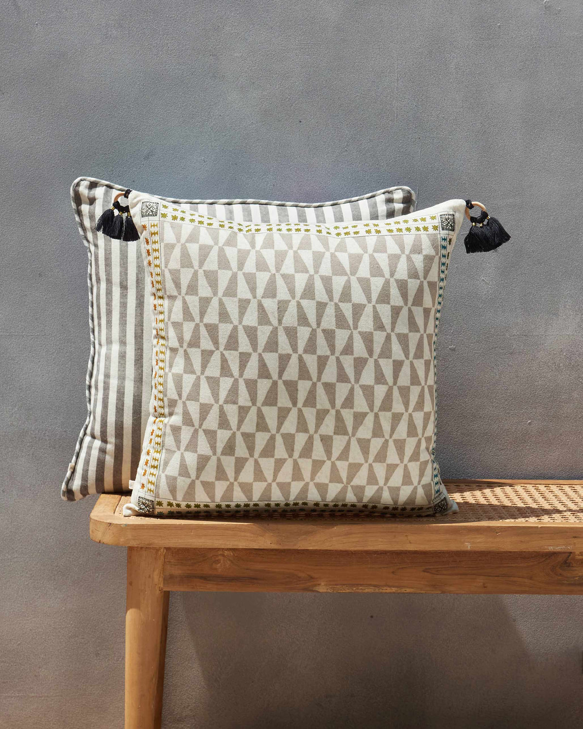 Cream and grey triangle-patterned cushion with a yellow stitched border on a wooden bench.