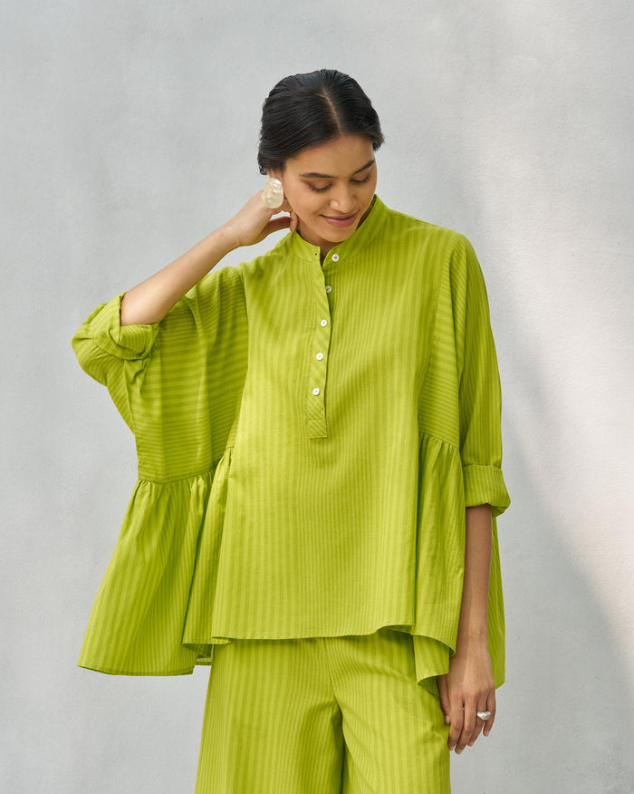 Person wearing a lime Dolman top with a stand collar and buttoned placket.