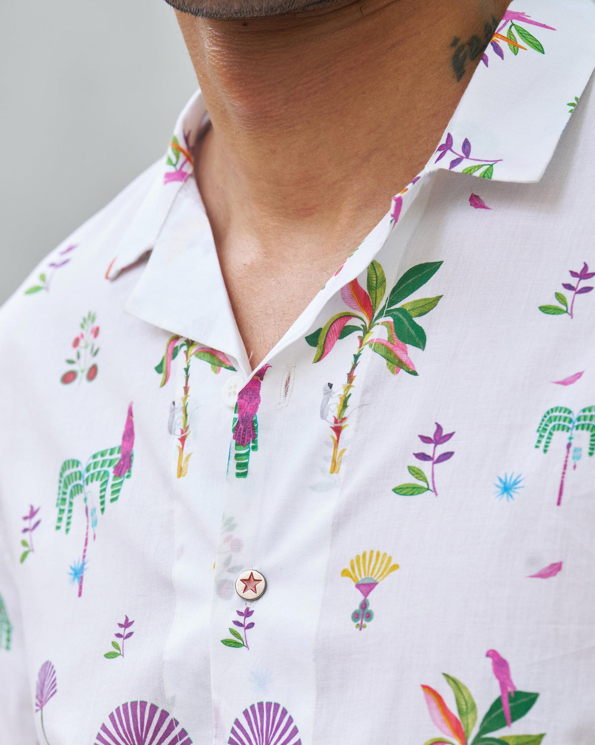 Close-up of a white Mistari shirt collar showing palm tree and bird motifs and a red star button.