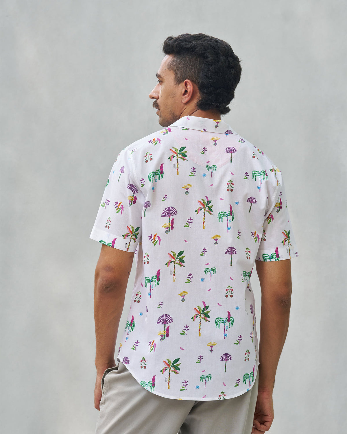 Back of a white Mistari shirt with palm tree and bird motifs worn by a person.