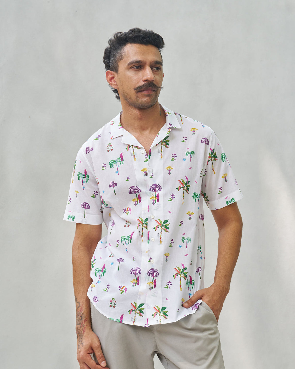 Half-length view of a white Mistari shirt with palm tree and bird motifs worn by a person.