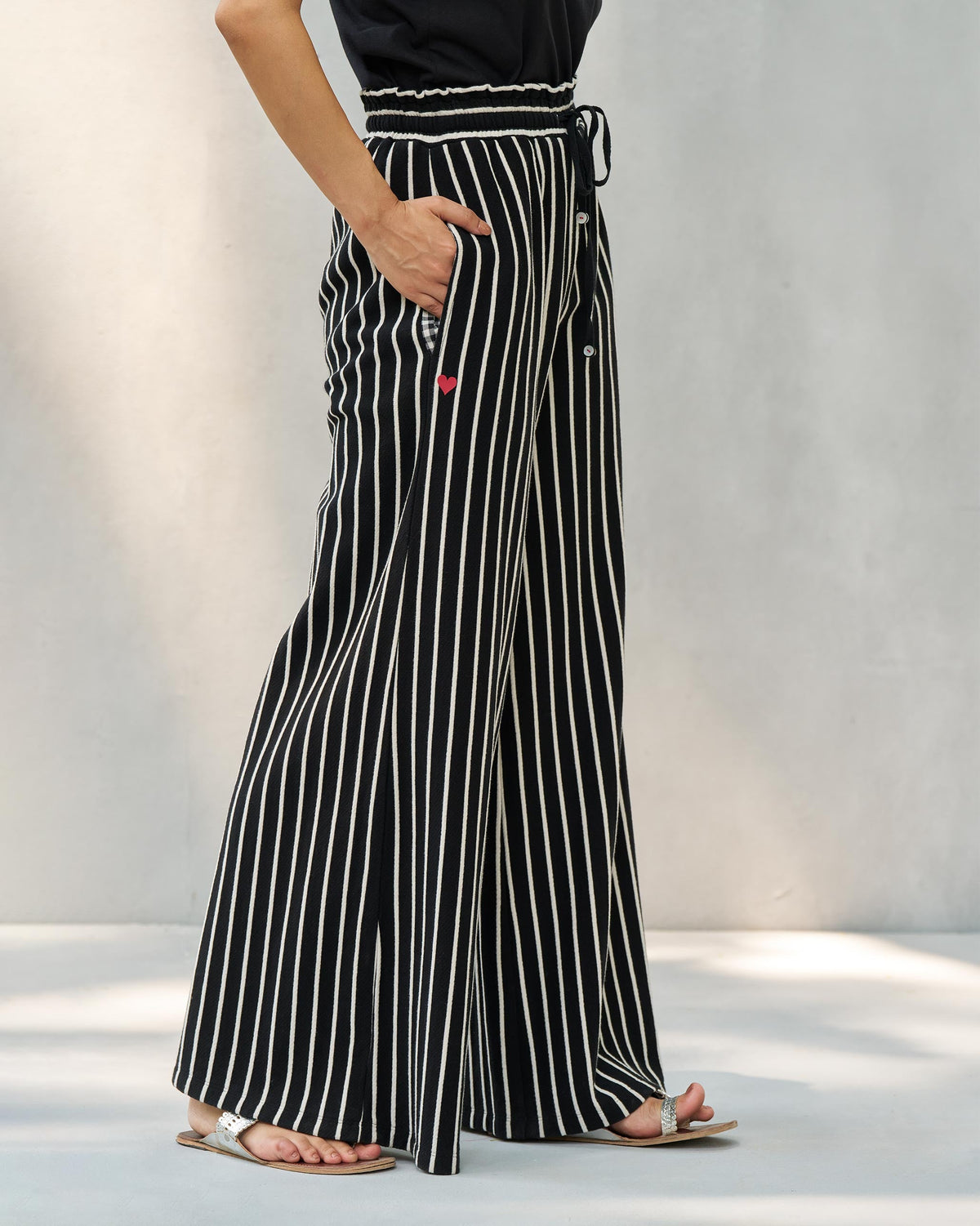 Side view of black and beige striped Nova pants with a pocket and red heart.