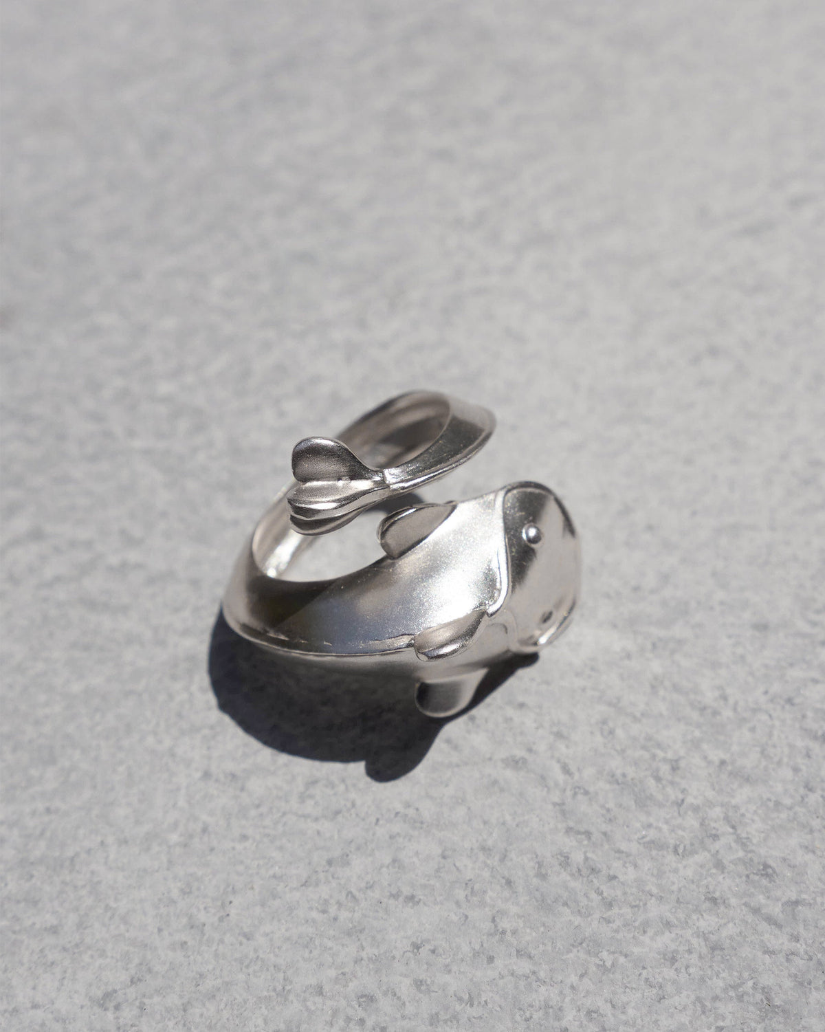 Three-quarter view of a silver Mud-Fish ring on a grey surface.