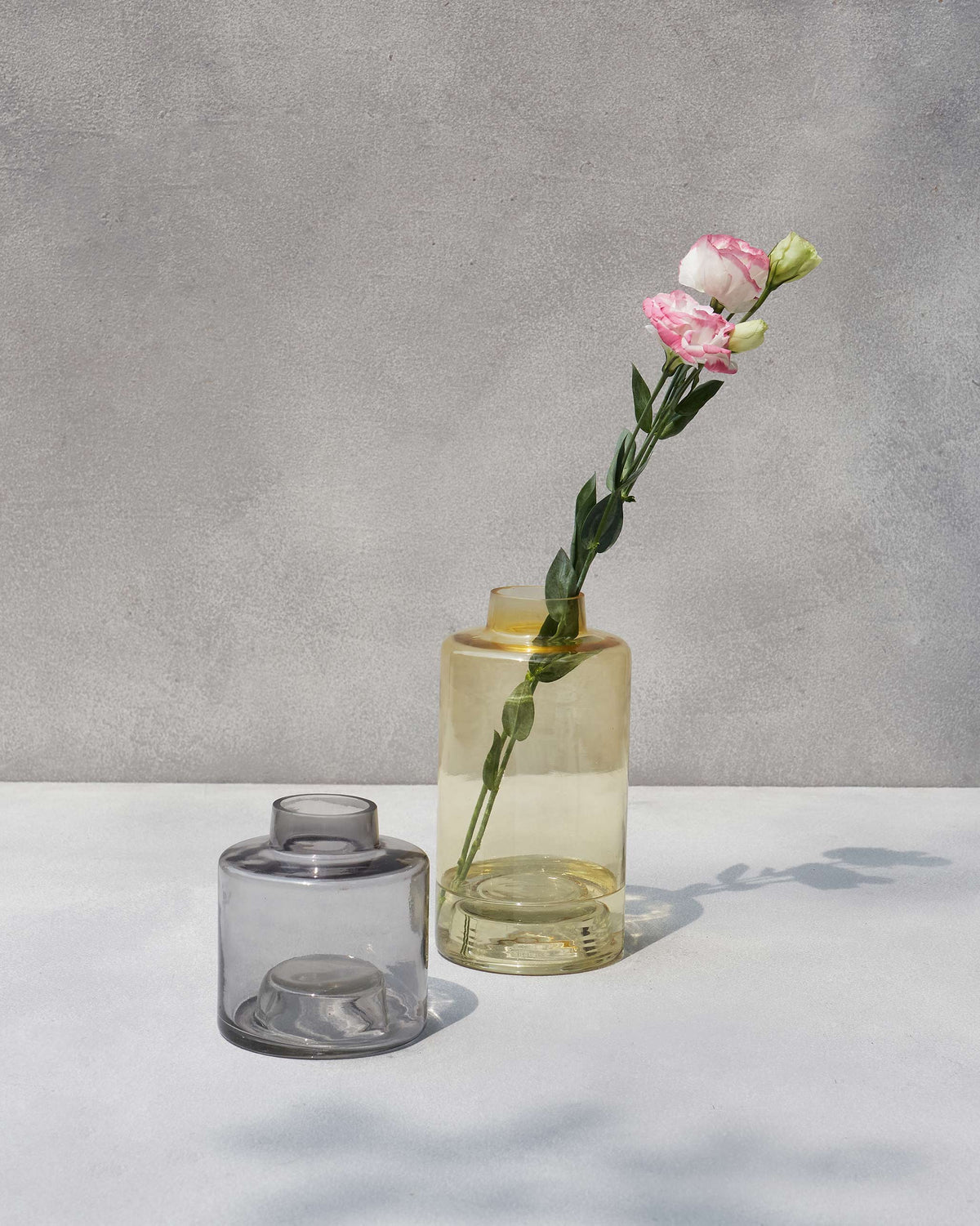 Grey and amber Azraq stackable vases on a pale surface, the amber one taller.