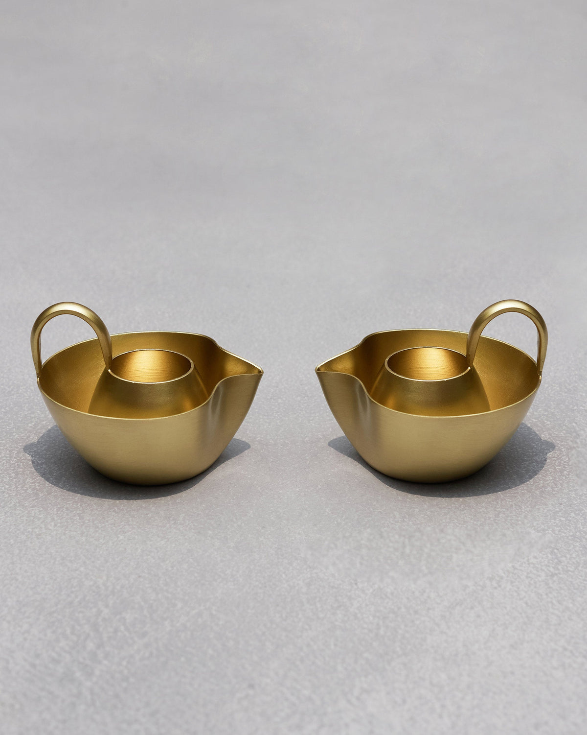 Pair of Asfar Diya standing side by side, each with a handle and spout.