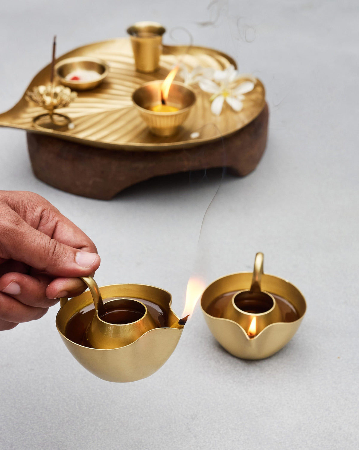 Hand lighting an Asfar Diya beside a second lit diya.