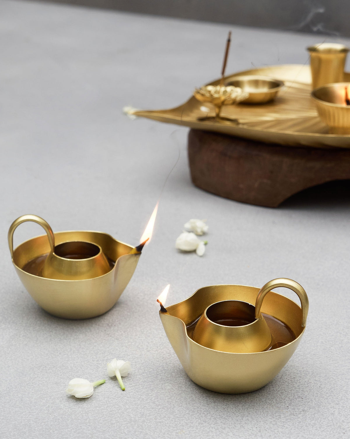 Two lit Asfar Diya with flames, with white flowers beside them.