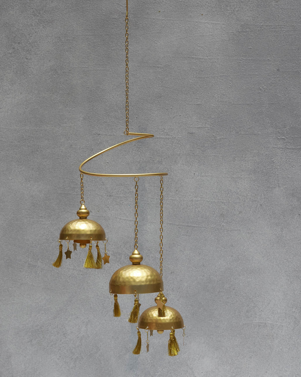 Asfar Windchime hung from a curved arm, its three bells at uneven heights.