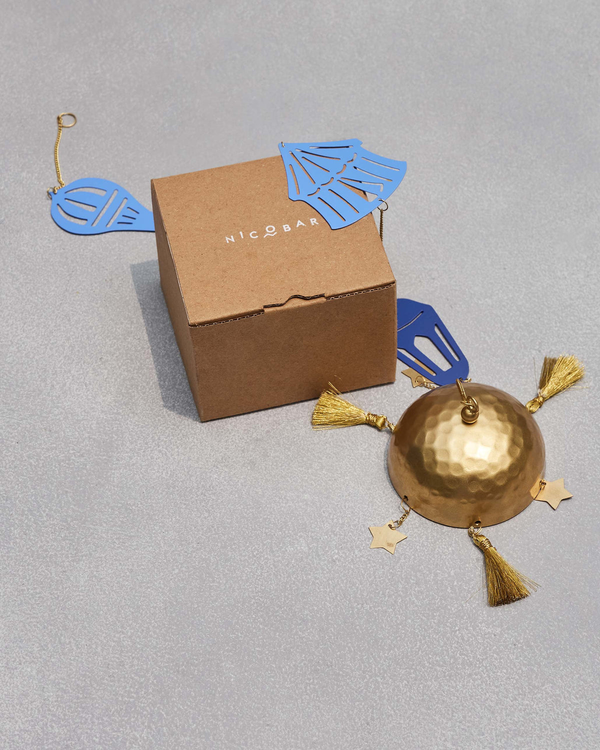 Azraq Toran laid out beside a kraft box, its blue motifs and brass bell with tassels.
