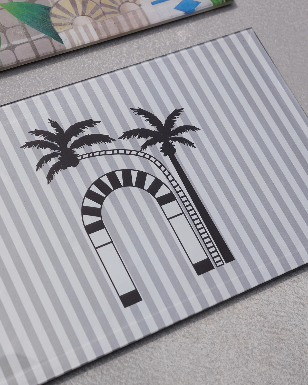 Close-up of a Sahara trivet with a black palm and arch motif on grey stripes.