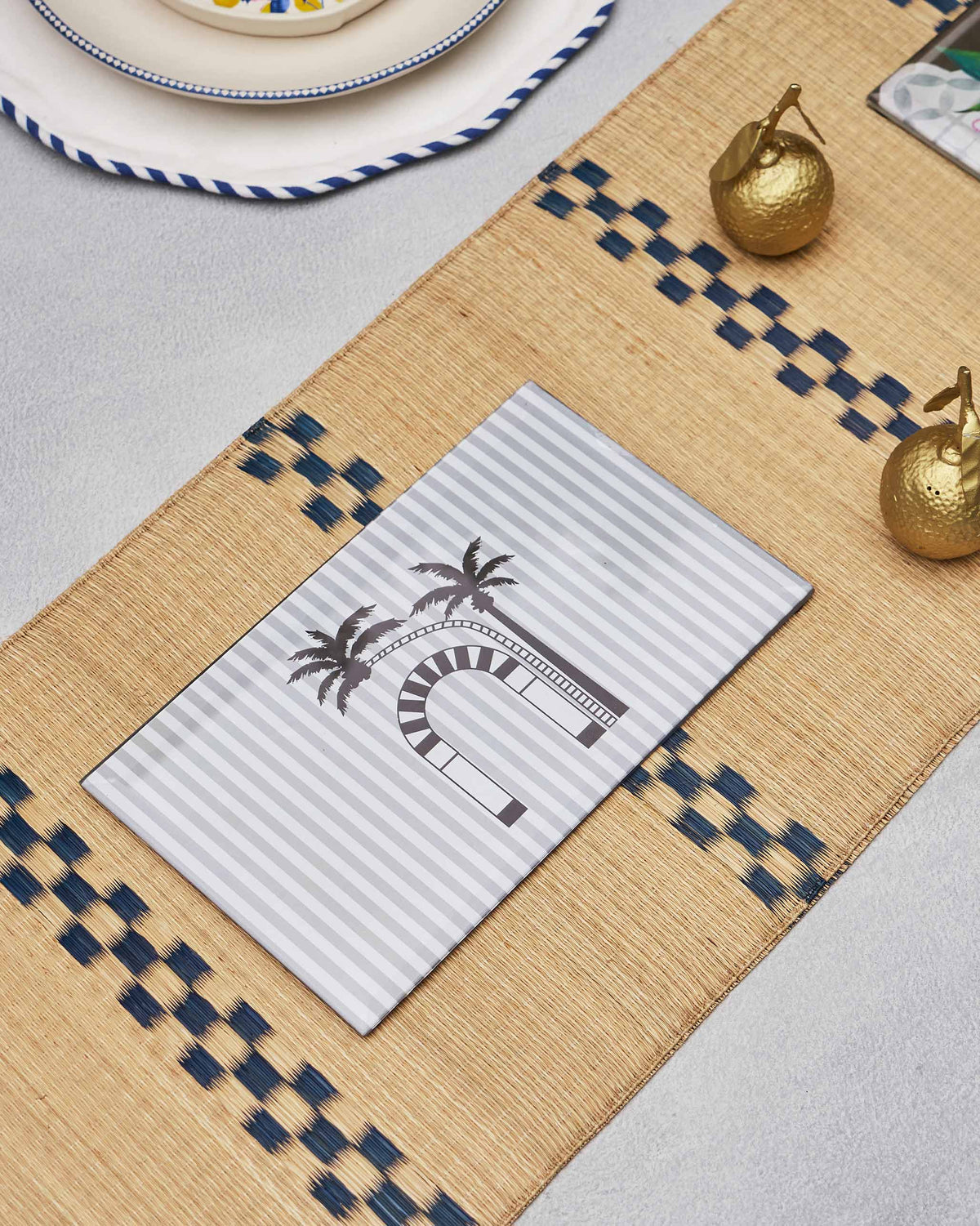 Striped Sahara trivet with a palm and arch motif on a woven table runner.