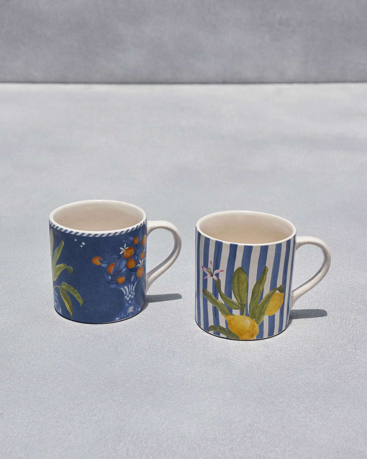 Asfar straight mugs showing navy citrus foliage and a striped lemon design.