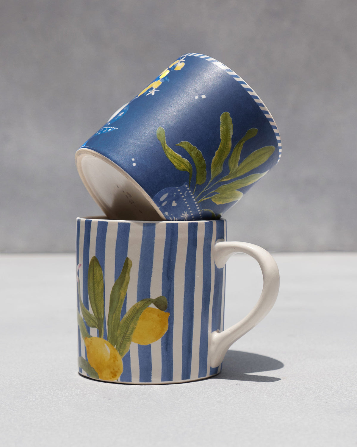 Stacked Asfar mugs showing the striped lemon design under a navy citrus mug.