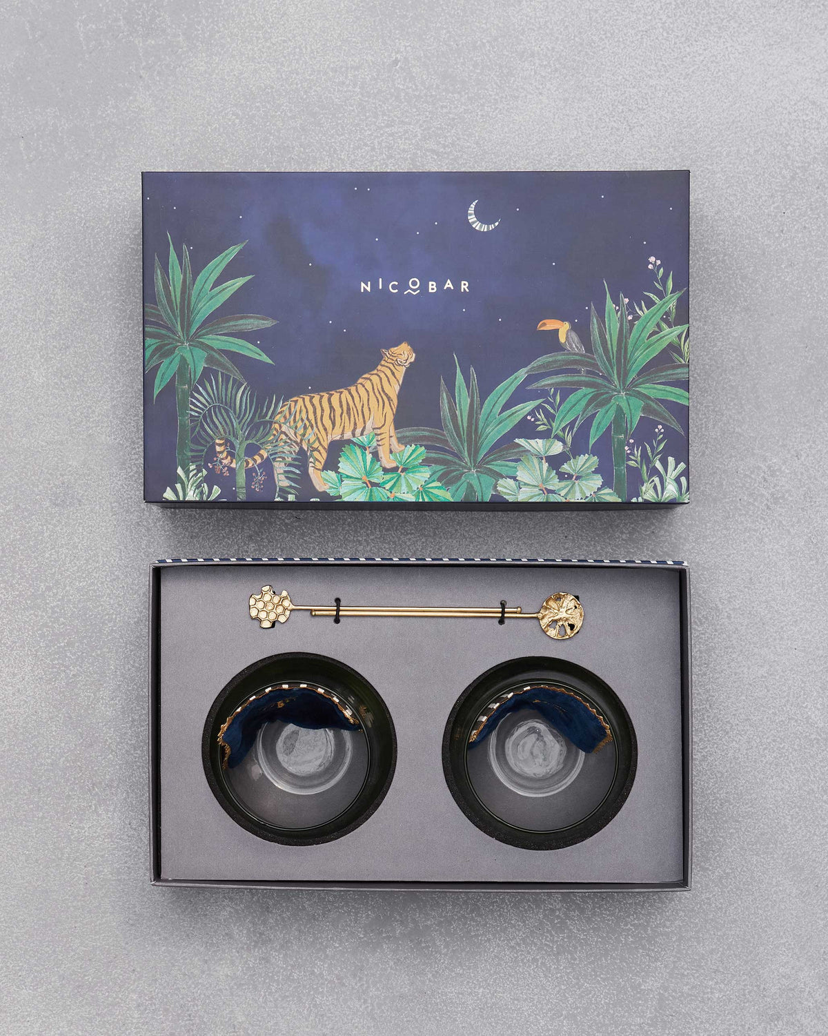 Open Azraq gift box showing navy coasters and two gold stirrers under the tiger lid.