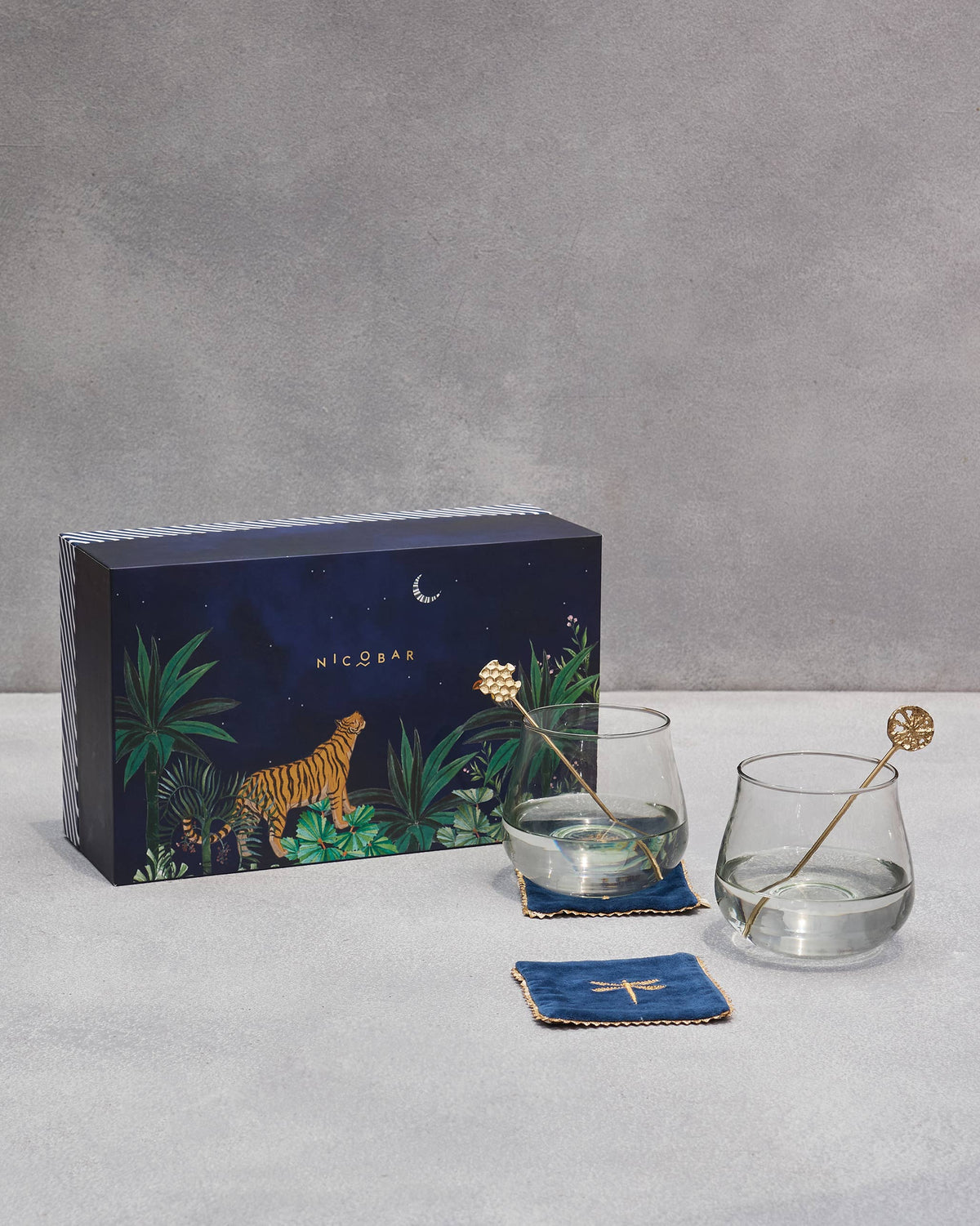 Azraq gift set with gin goblets, gold stirrers, and navy coasters by its tiger box.