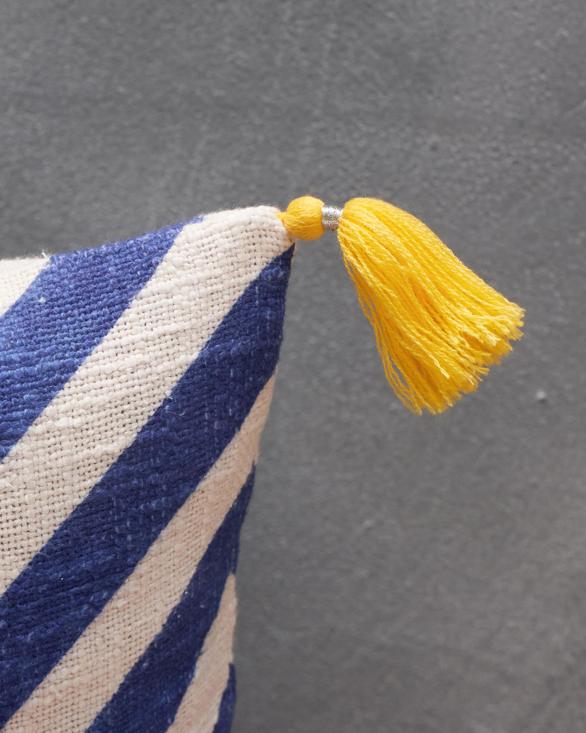 Close-up of Nizara Herring Cushion Cover - Indigo showing a yellow tassel on a corner.