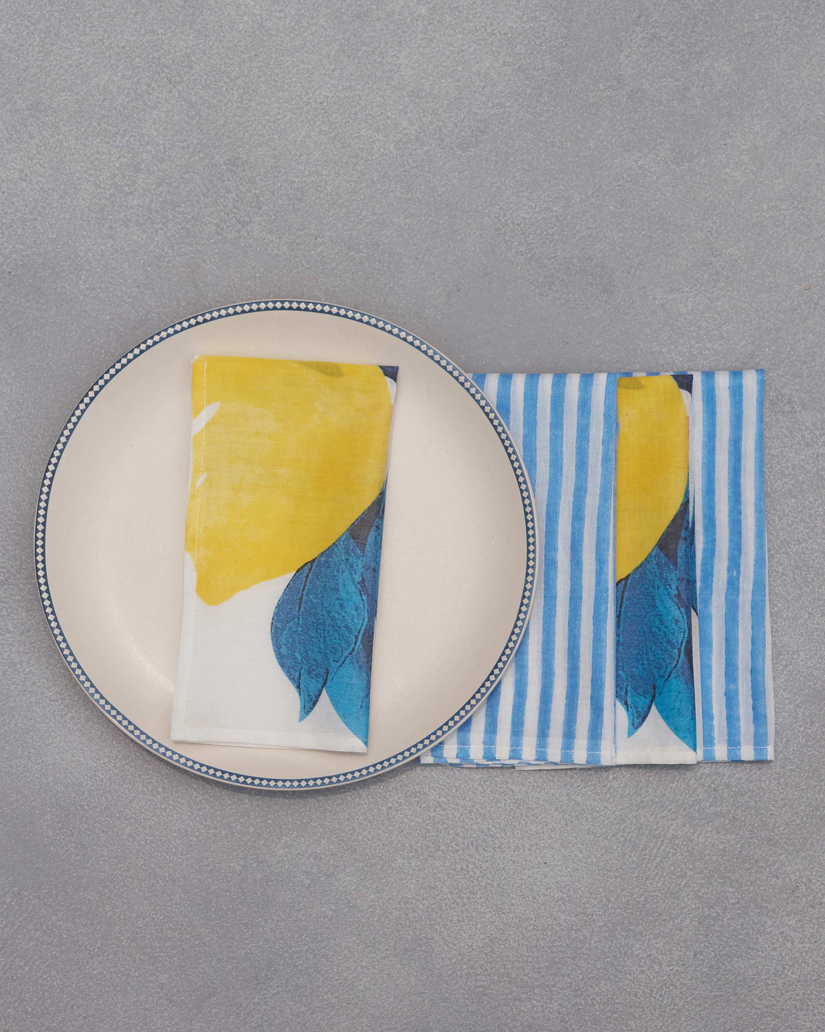 Azraq lemon-print napkin folded on a plate beside a striped napkin.