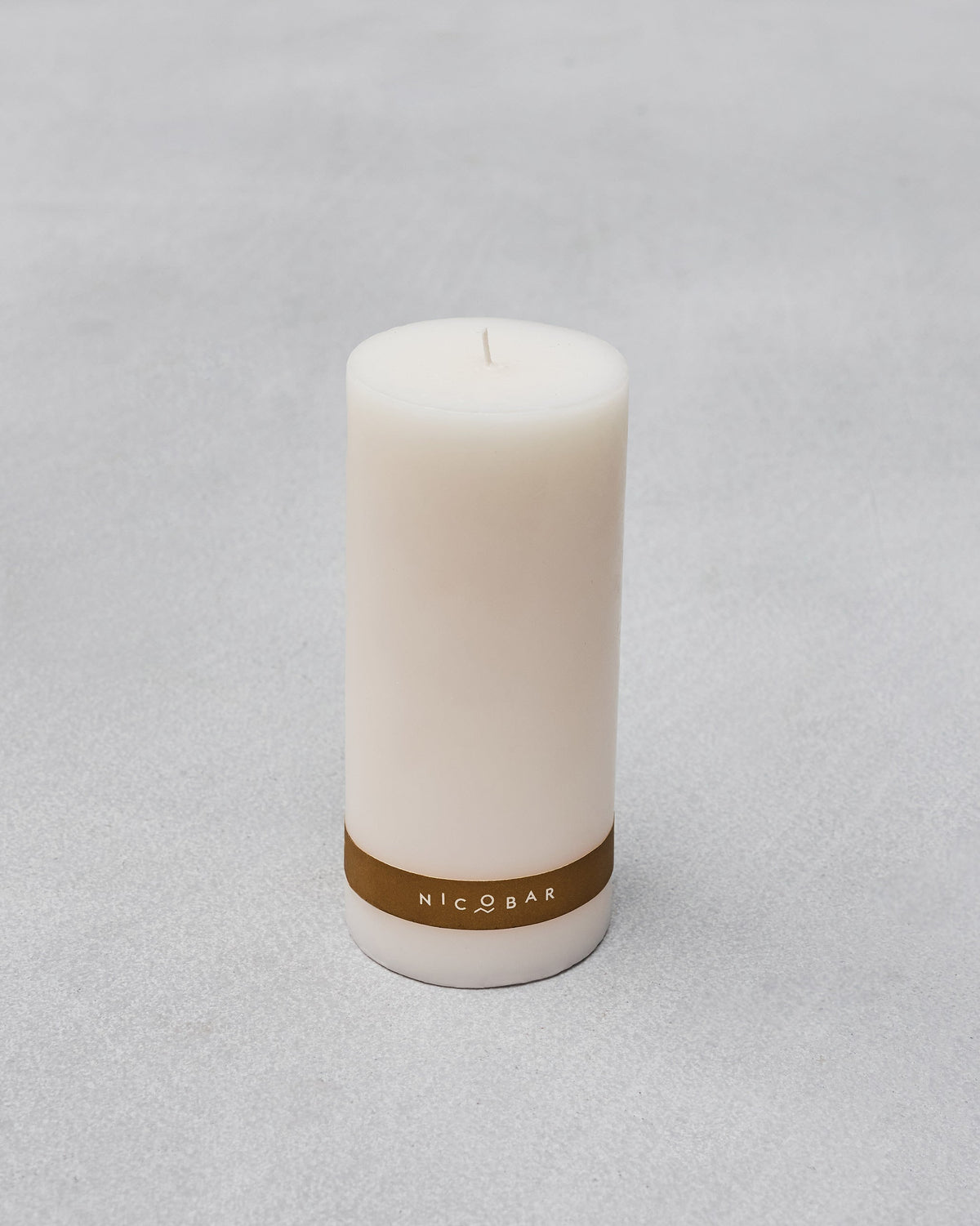 Casablanca Pillar Candle with a gold NICOBAR band on a grey surface.