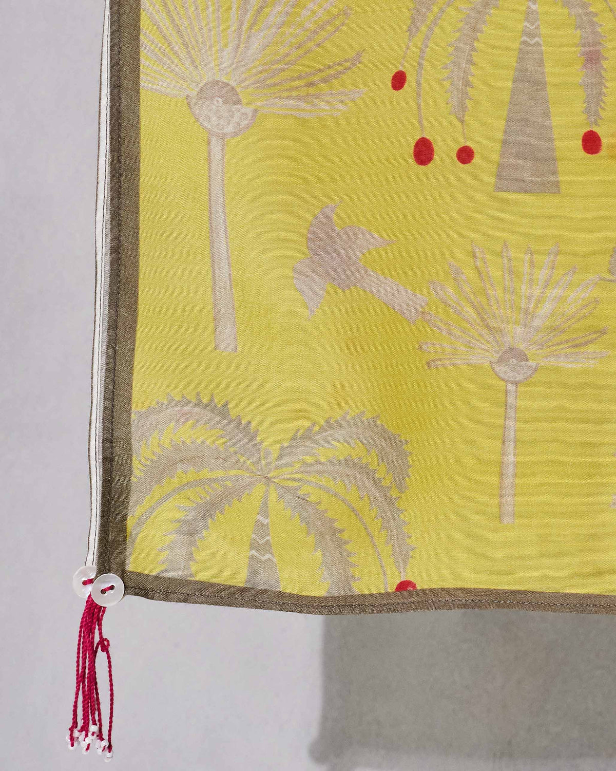 Close-up of Fleur Scarf corner showing its palm tree print and red tassel.