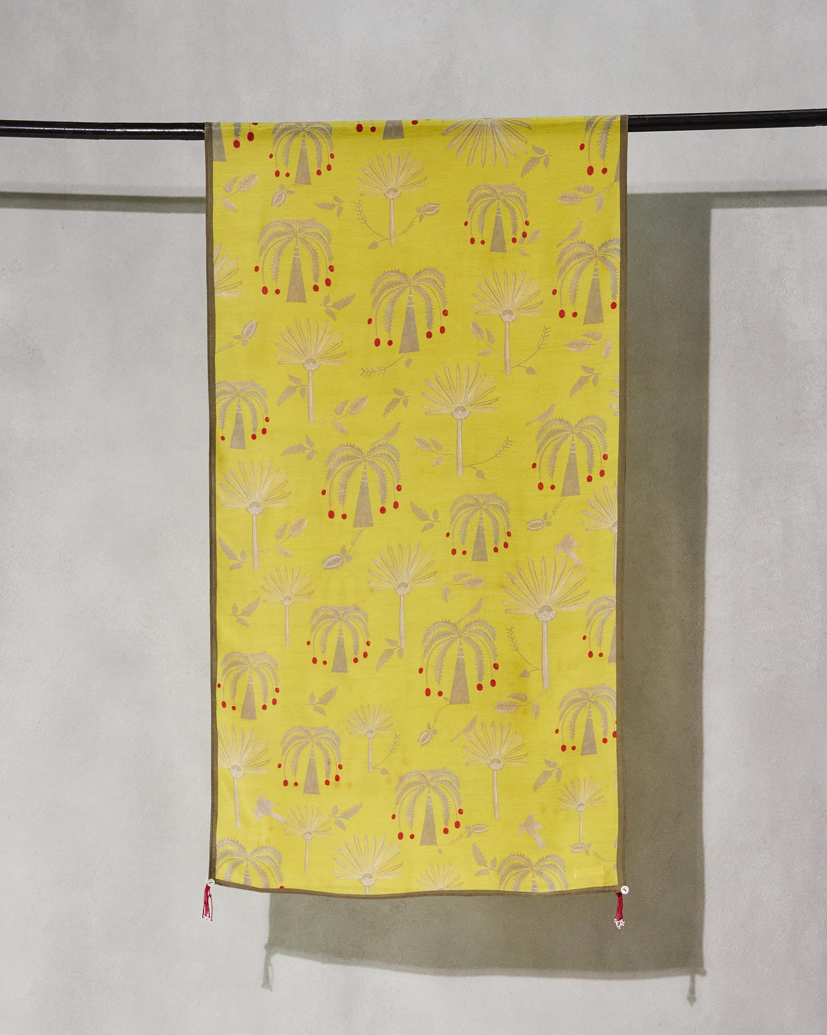 Fleur Scarf hung on a rod, yellow with a palm tree print.