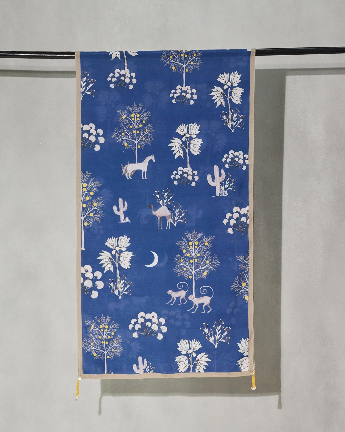 Willow Scarf hung on a rail, showing its blue field of ivory trees and animals.