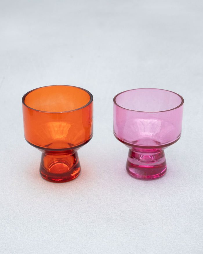 Pair of Mirage votives in orange and pink glass on a pale surface.
