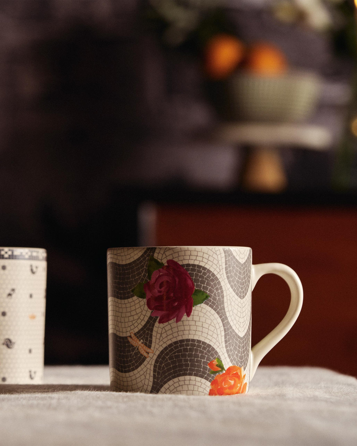 Mosaic Bloom straight mug with rose motifs sitting on a linen tablecloth.