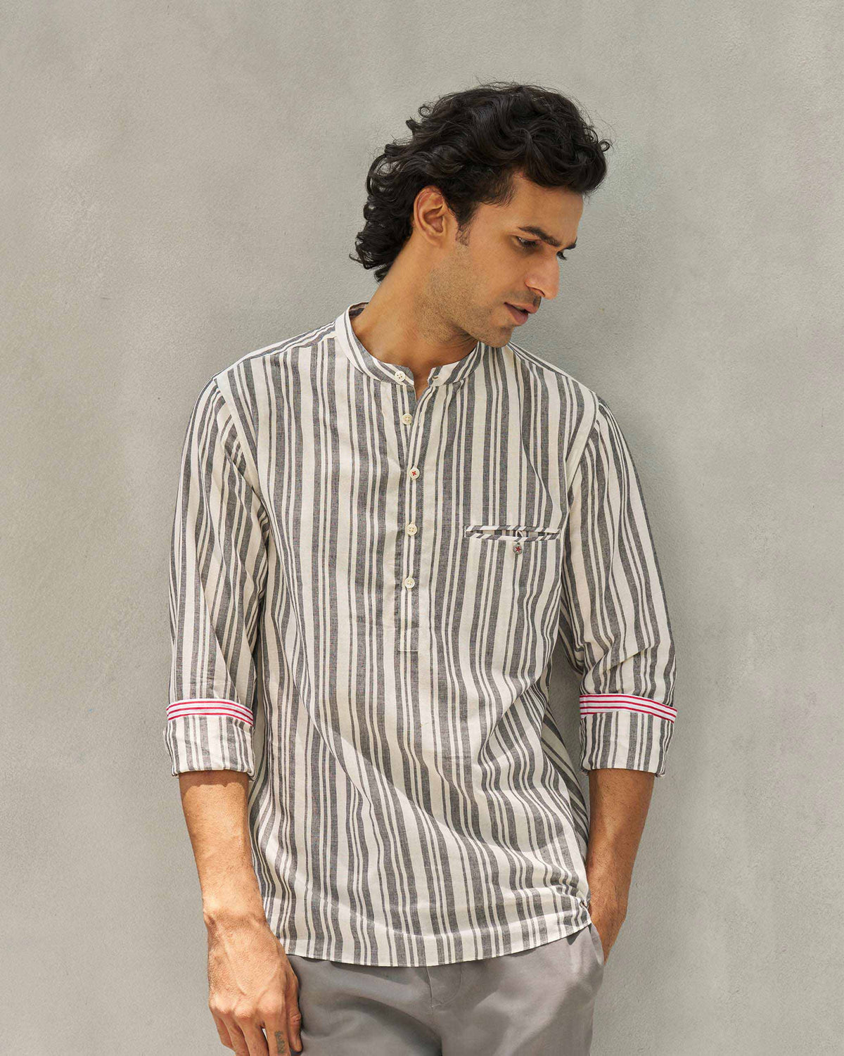 Person wearing a striped Pondicherry Shirt in ivory and grey with red-trimmed cuffs.