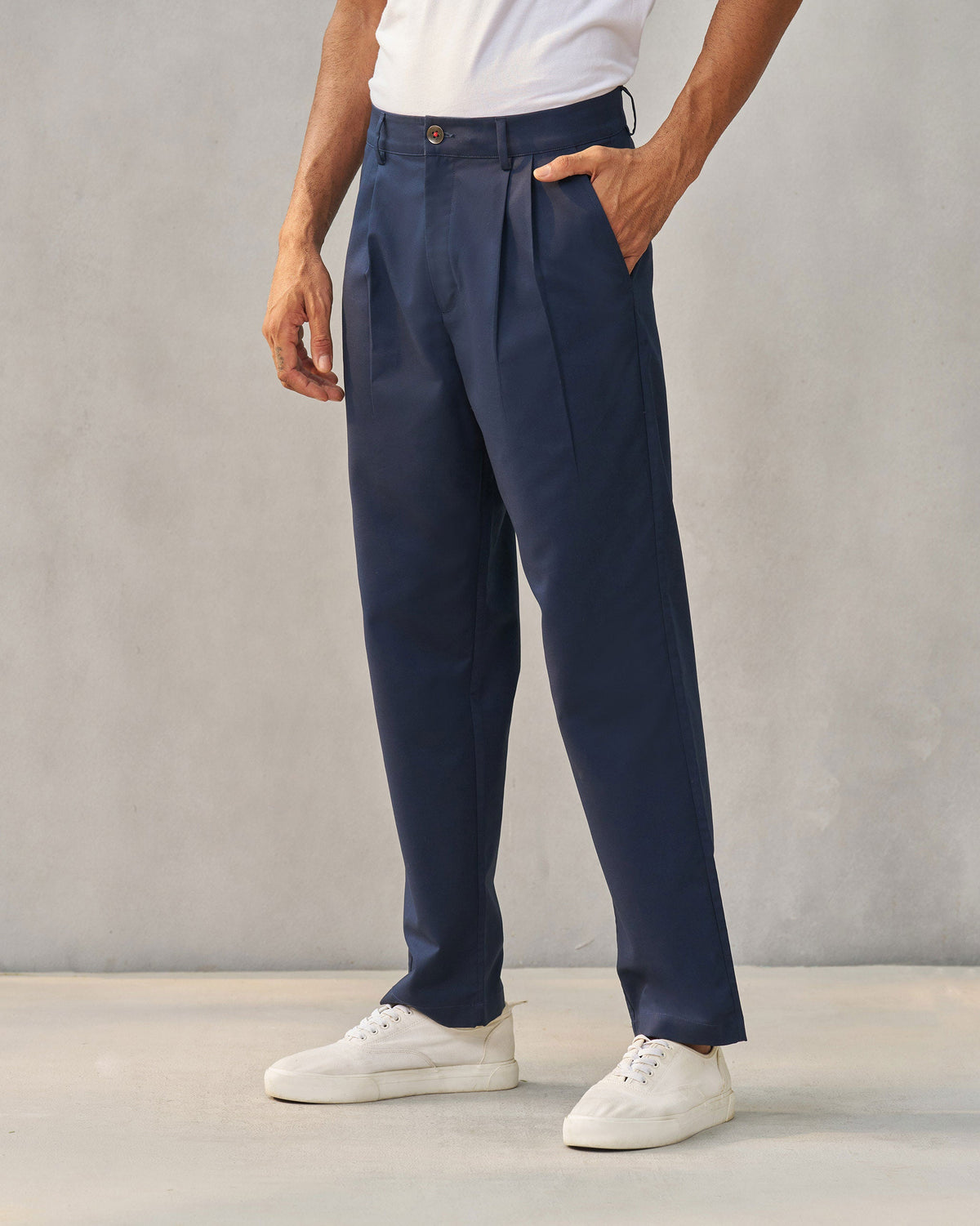 Person wearing navy Forty Trousers with pleats, one hand in a pocket.