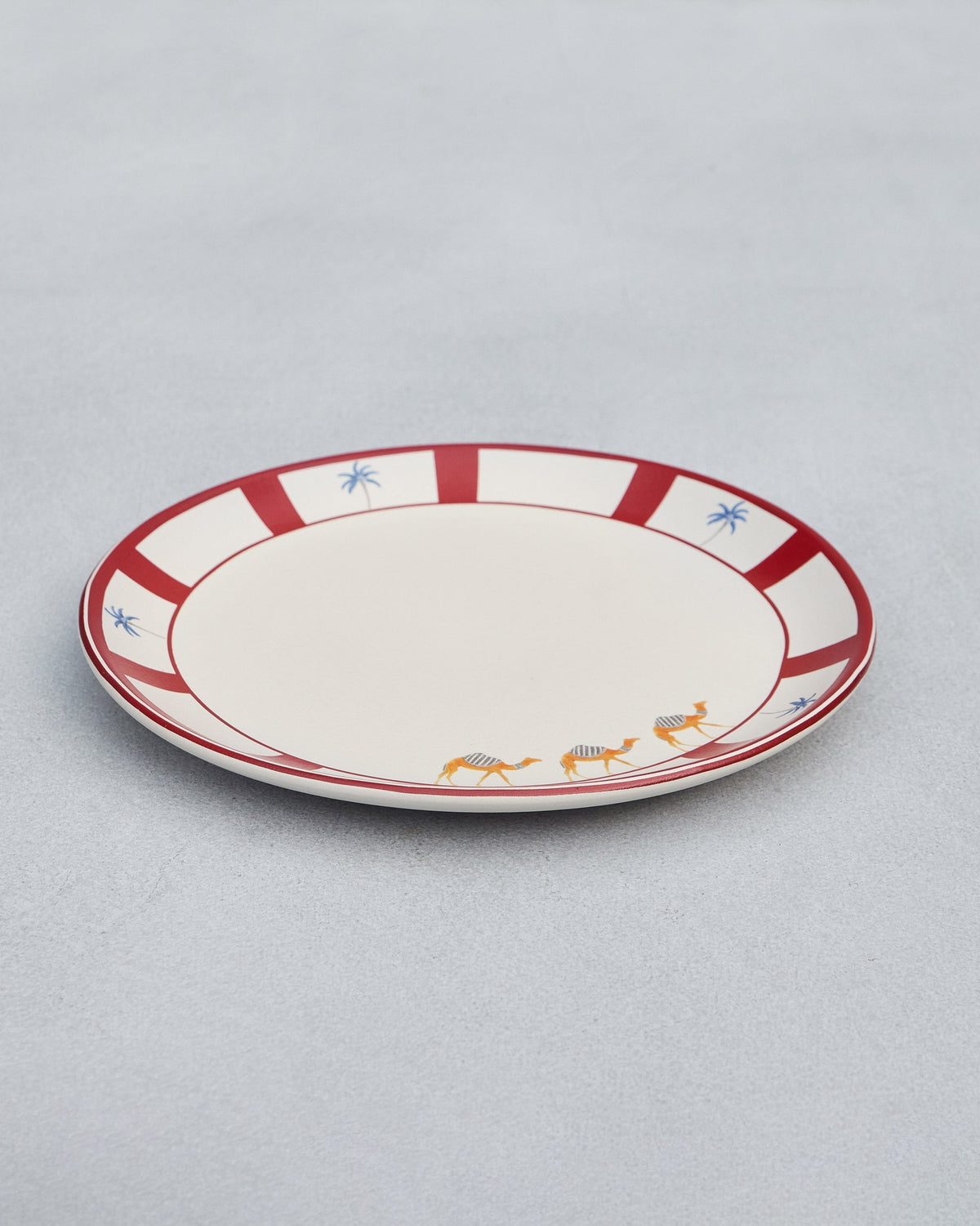 Desert Trail Dinner Plate with a red rim, angled on a grey surface.