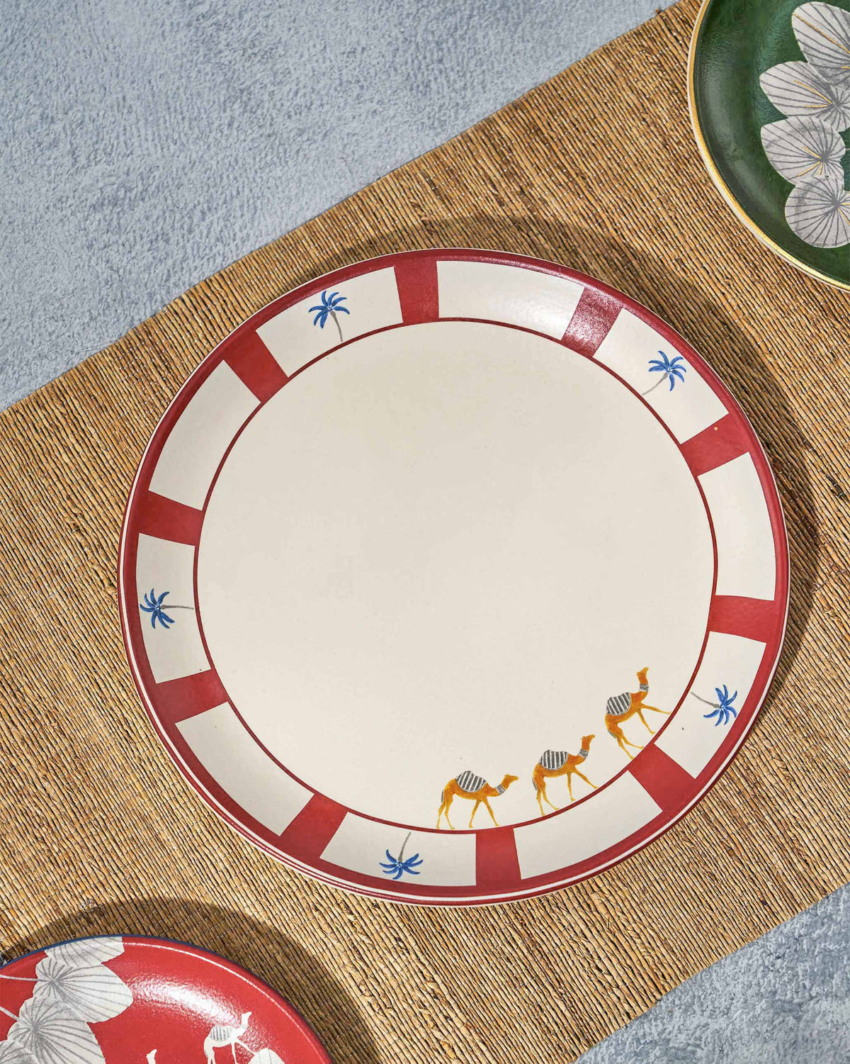 Desert Trail Dinner Plate with camels on its red rim, styled with other plates.
