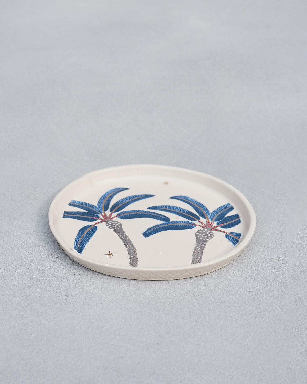Dancing Palm Dessert Plate at an angle, with blue palm trees on a cream glaze.
