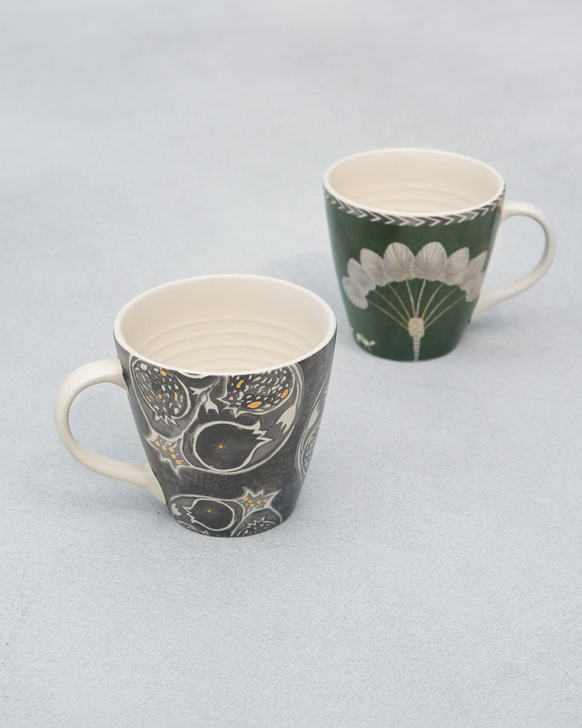Pair of Anar Palm Conical Mugs standing side by side on a grey surface.