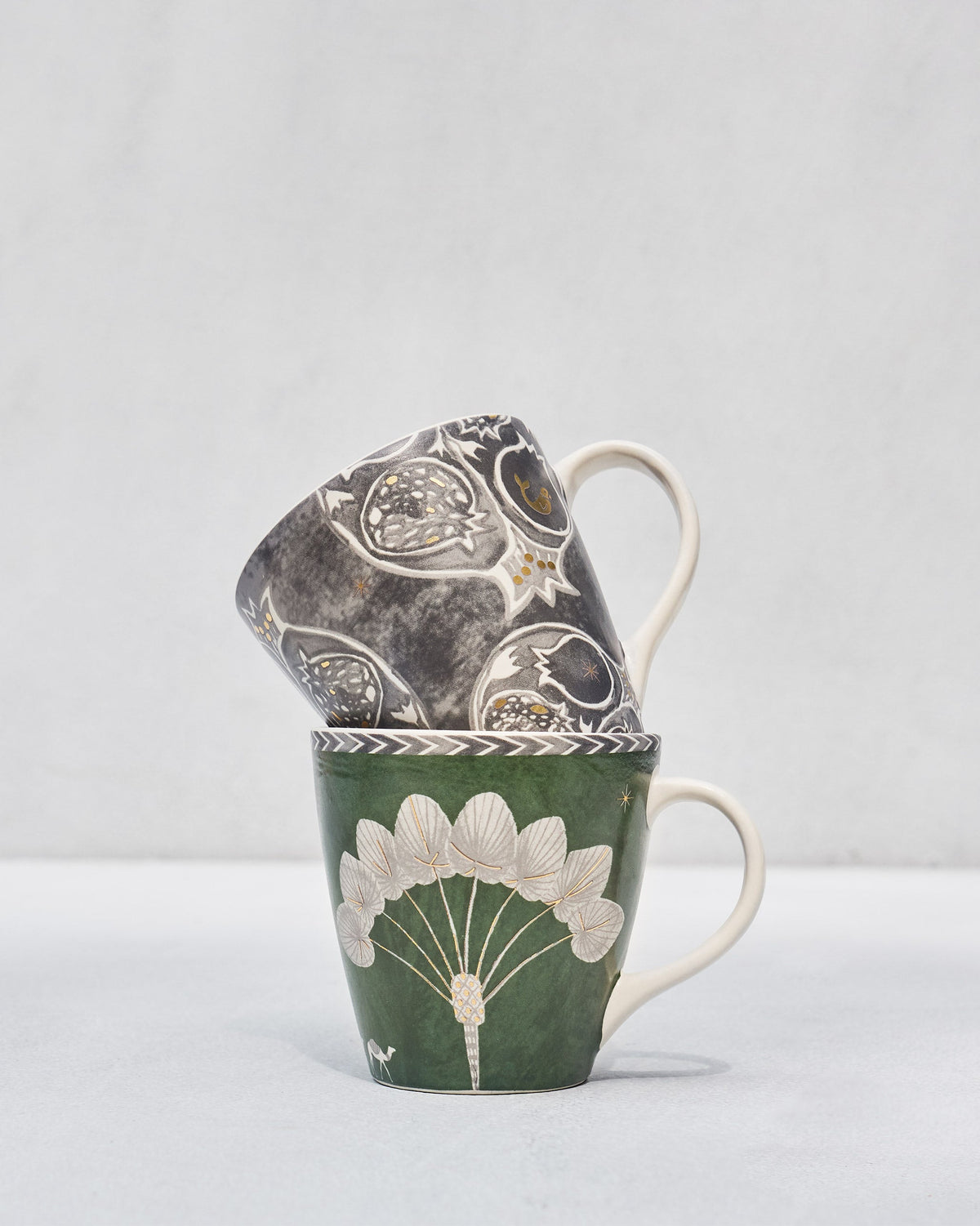 Anar Palm Conical Mugs with the charcoal mug tilted behind the green mug.