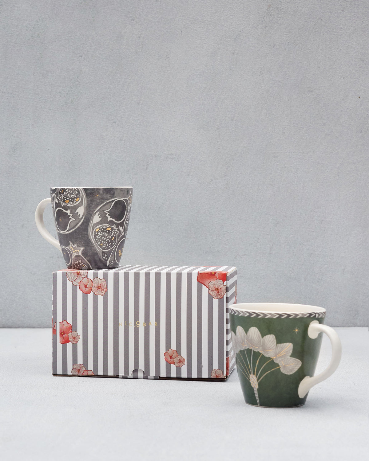 Anar Palm Conical Mugs with one charcoal mug on a striped gift box.